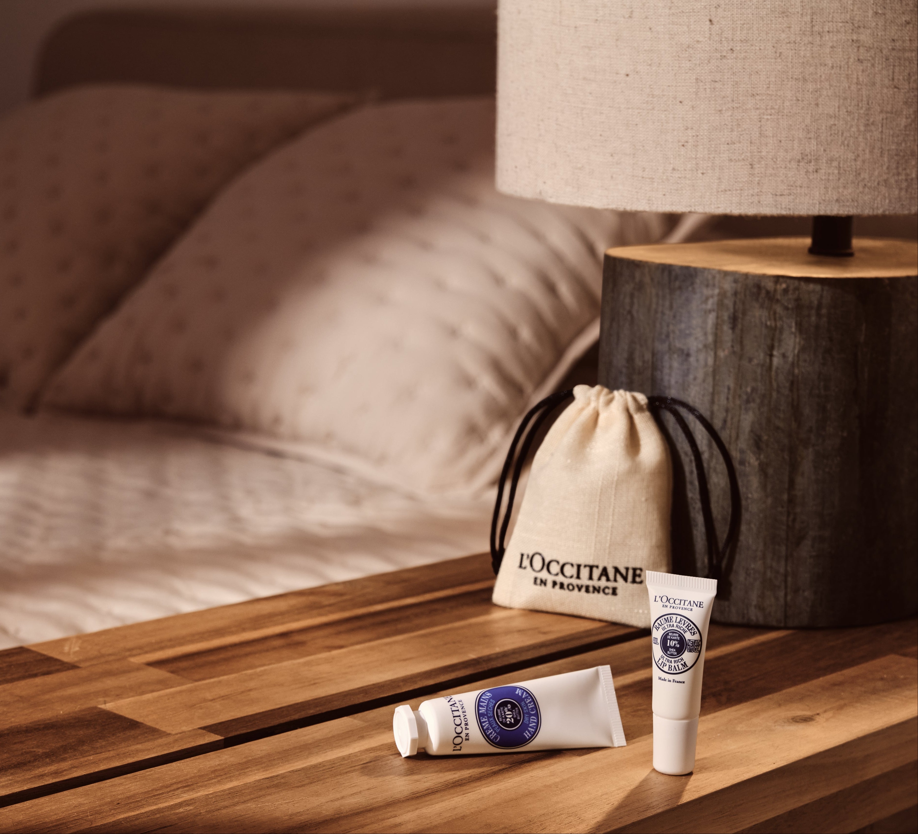 L'Occitane products on a wooden surface with a bed in the background
